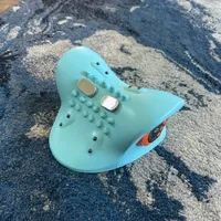 Imagem enviada pelo cliente. Clique para ver mais detalhes. A imagem representa: Um brinquedo ou controlador azul claro em forma de arraia com botões e alças texturizadas sobre um tapete estampado