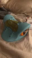 Imagem enviada pelo cliente. Clique para ver mais detalhes. A imagem representa: Sapato Blue Crocs em uma cama com o que parece ser um picles ou objeto verde colocado em cima